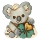 Mini koala Thun in ceramica color grigio chiaro e beige con occhi neri e naso scuro, che tiene in grembo un quadrifoglio verde e oro.