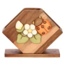 Portatovaglioli THUN in legno di acacia con struttura a V, decorato con una coccinella in ceramica e fiori bianchi sulla facciata frontale, su sfondo bianco.