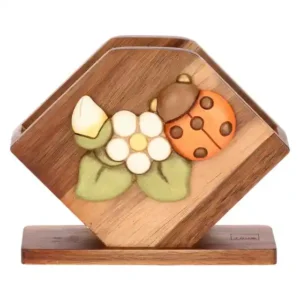 Portatovaglioli THUN in legno di acacia con struttura a V, decorato con una coccinella in ceramica e fiori bianchi sulla facciata frontale, su sfondo bianco.