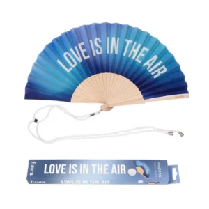 Ventaglio pieghevole con tessuto a gradiente che sfuma dal blu scuro all'azzurro chiaro, con stecche in legno chiaro. Sul tessuto è stampata in bianco la frase 'LOVE IS IN THE AIR'. Un cordino bianco è adagiato sotto il ventaglio, accanto alla sua scatola di imballaggio coordinata che riporta la stessa frase e il logo 'fisura'