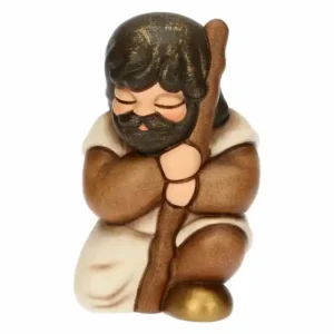 Statuina in ceramica Thun del Presepe Classico raffigurante un pellegrino inginocchiato con tunica marrone, bastone e dettagli dorati.